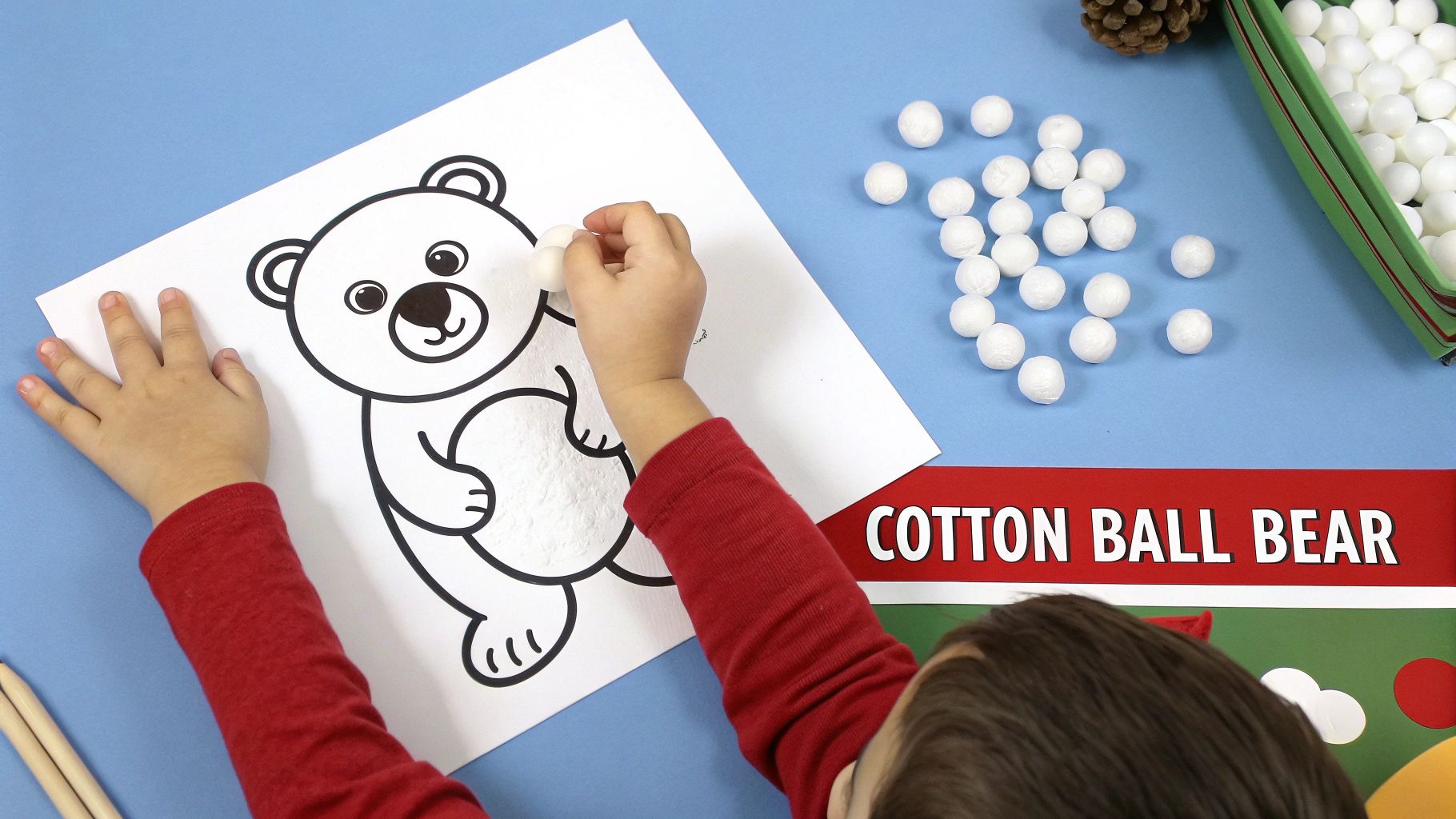 A child's hands busy gluing white cotton balls onto a polar bear drawing for a craft activity.