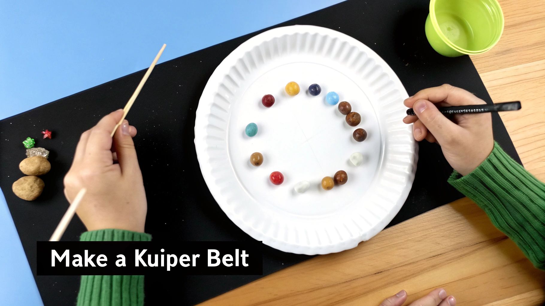 Hands arranging colorful beads on a white paper plate, making a Kuiper Belt model for a craft project.