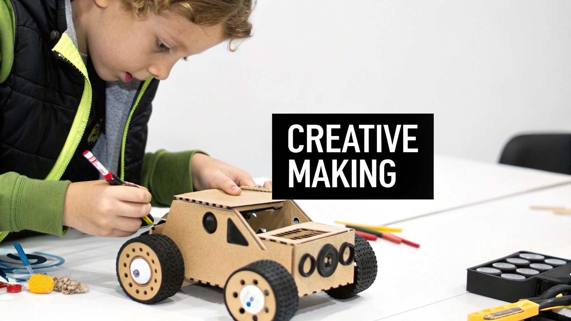 A young boy, focused, decorates a cardboard model car on a white table, engaging in creative making.