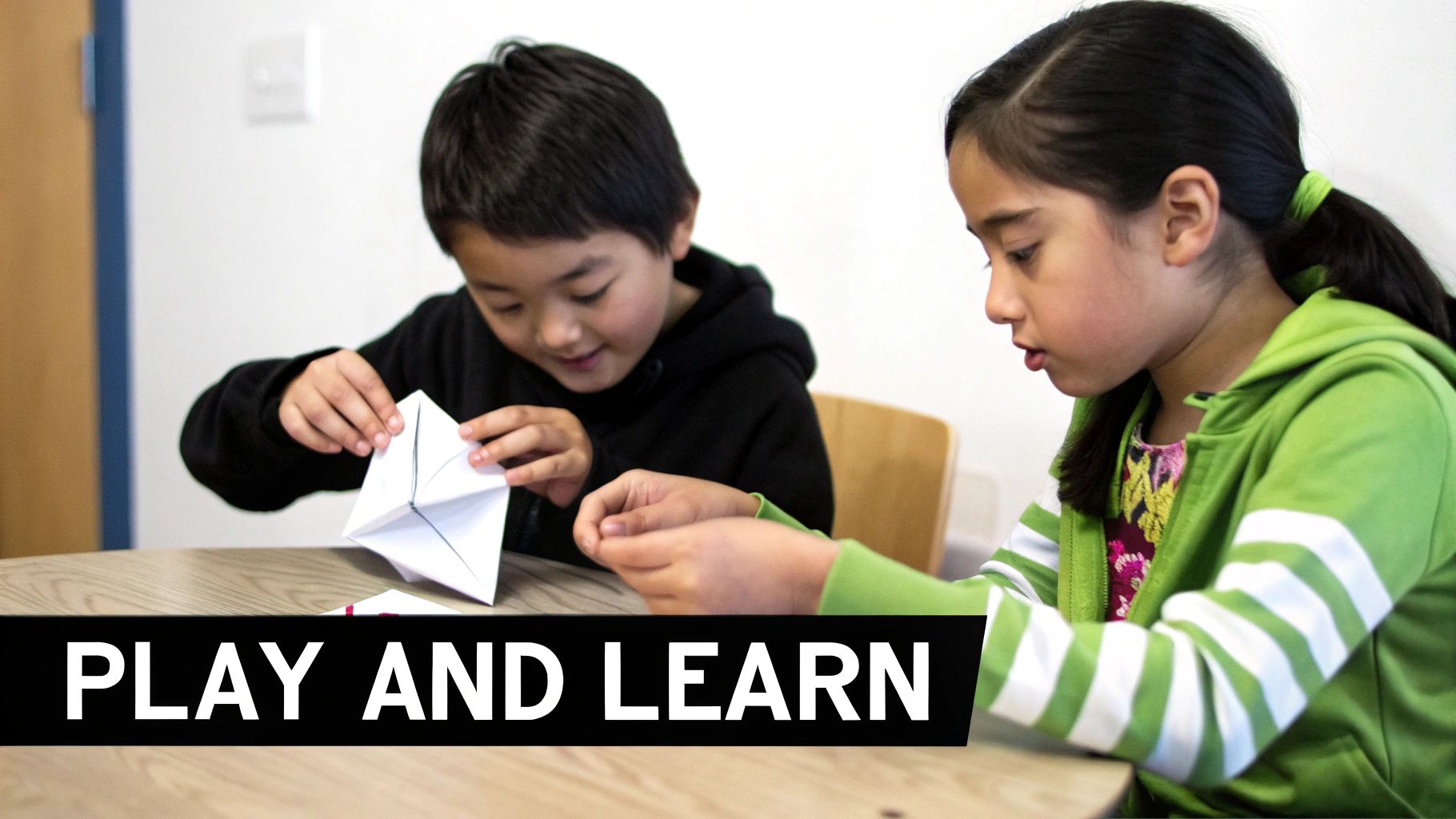 Two focused children are happily engaged in folding white paper, possibly making a chatterbox, at a wooden table.