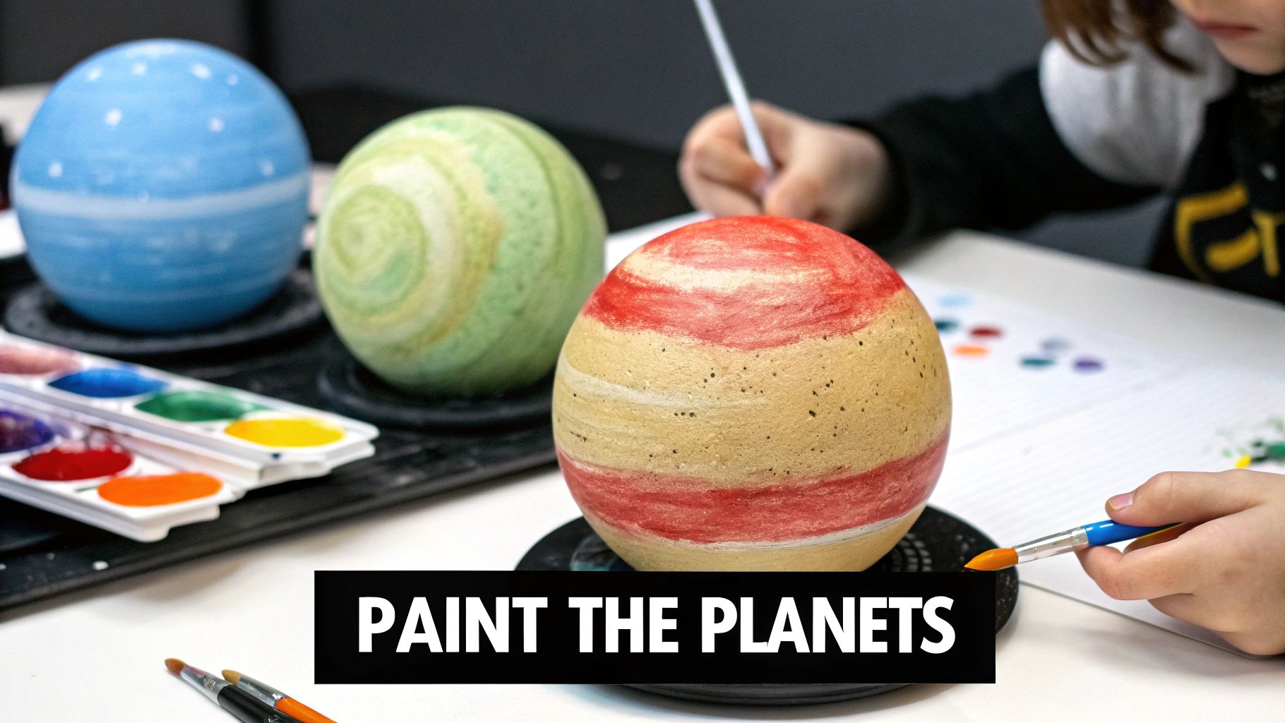 A child paints model planets with watercolors, featuring blue, green, and red-striped spheres.