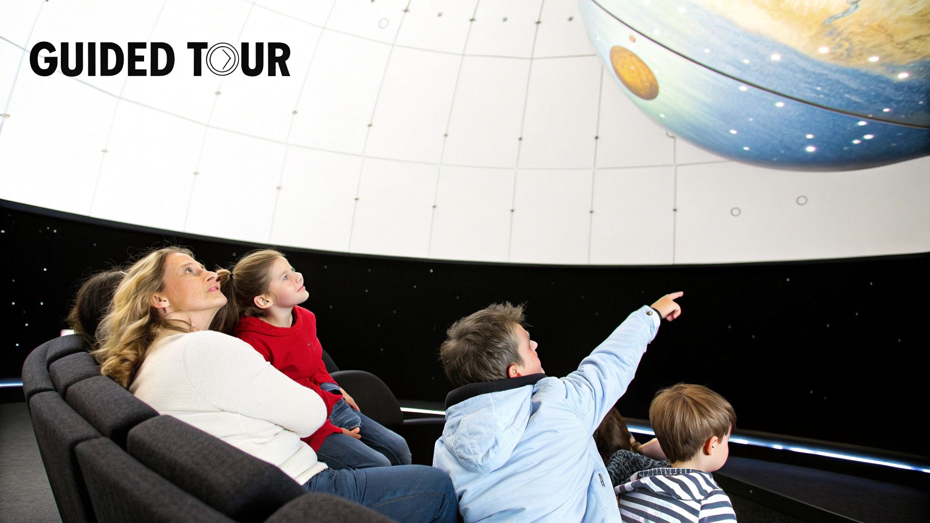 A family on a guided tour in a planetarium, looking up at a large illuminated globe.