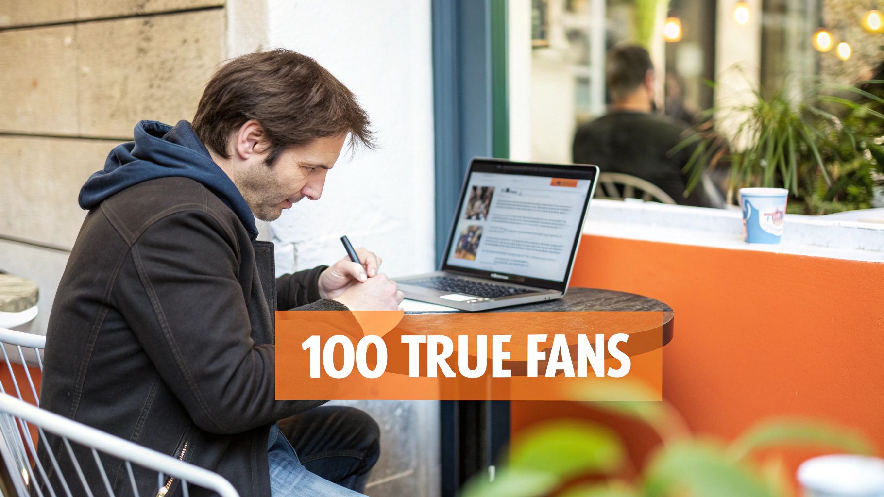 A man writing notes next to a laptop at an outdoor cafe with a text overlay: "100 TRUE FANS."