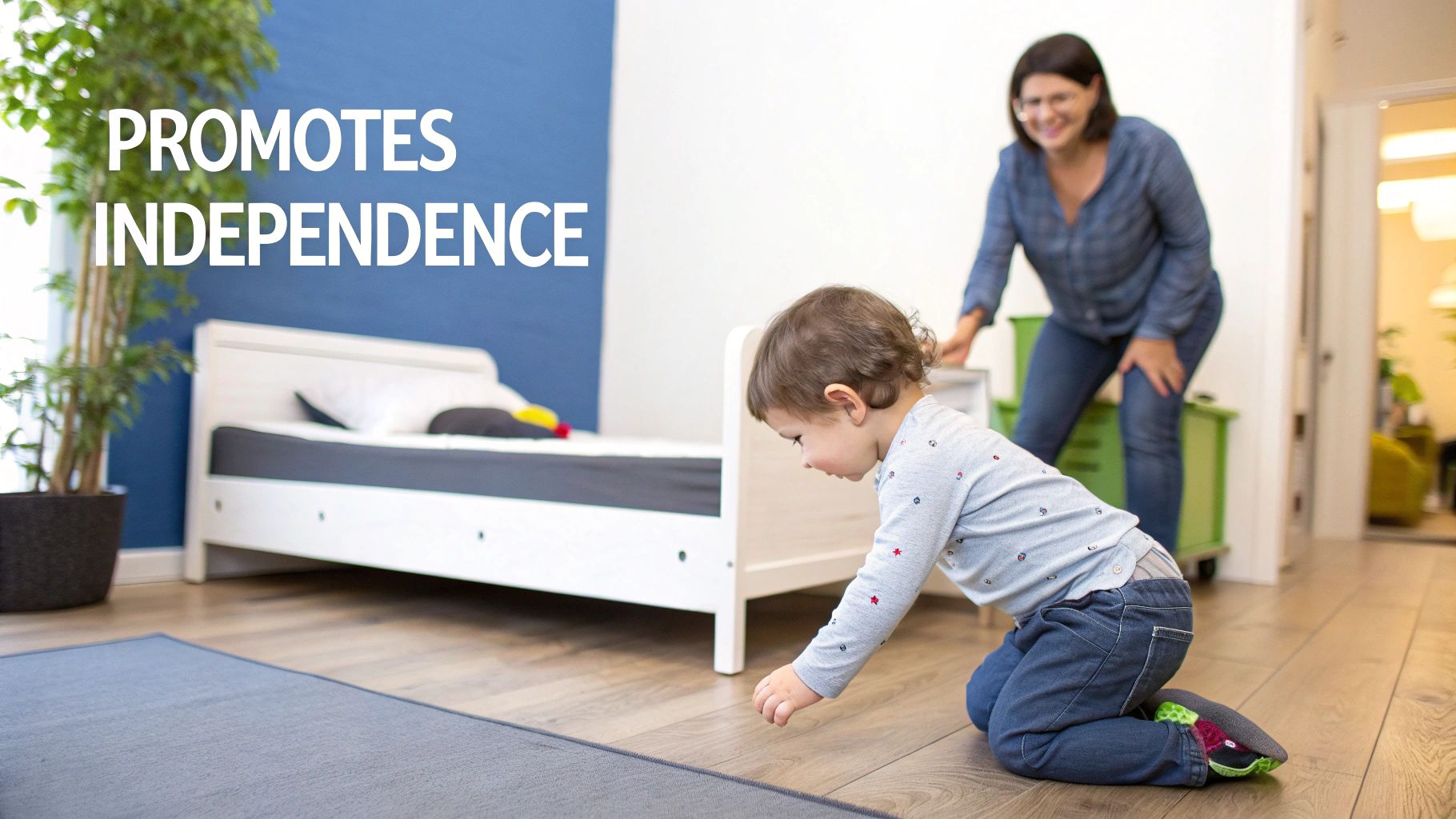 A young child kneels on the floor reaching out, with a low-to-the-ground bed nearby and a smiling woman observing.