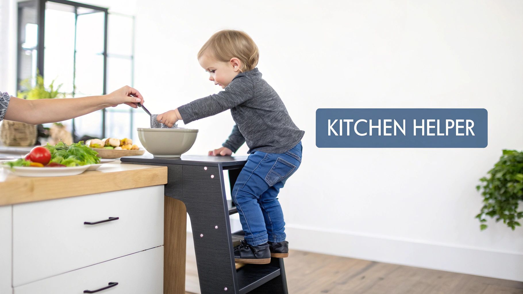 A toddler on a kitchen helper stool helps an adult prepare food, stirring ingredients in a bowl.