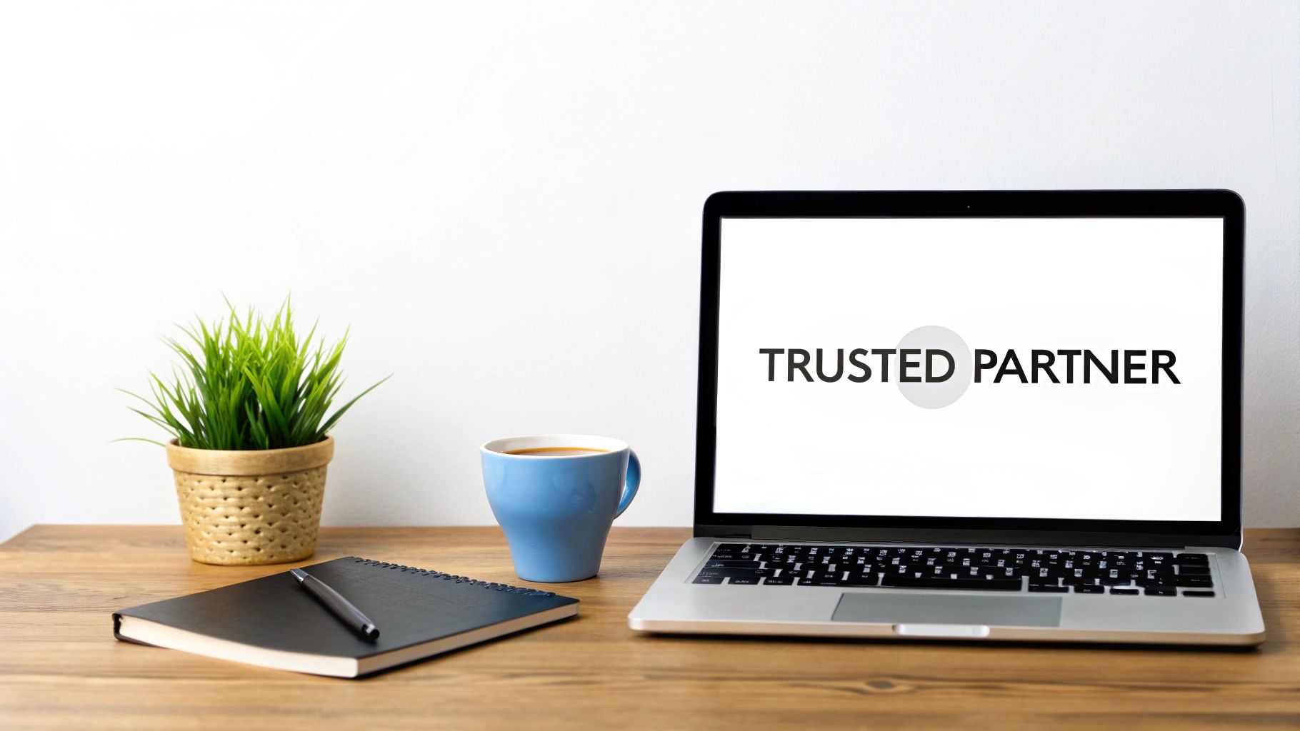 Clean office desk with a laptop displaying 'TRUSTED PARTNER', a potted plant, coffee, and notebook.