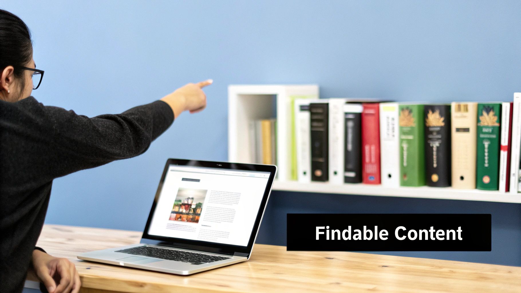 Person pointing at a bookshelf with a laptop displaying 'Findable Content' on a wooden desk.