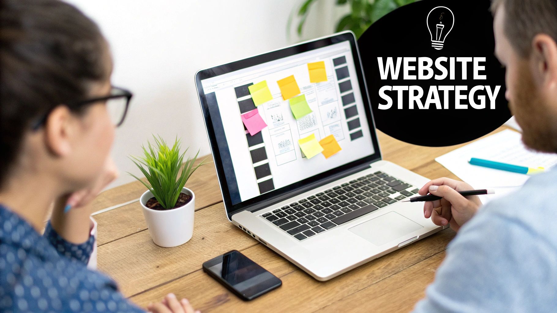 Two people collaborating on website strategy, looking at a laptop with a wireframe and sticky notes.