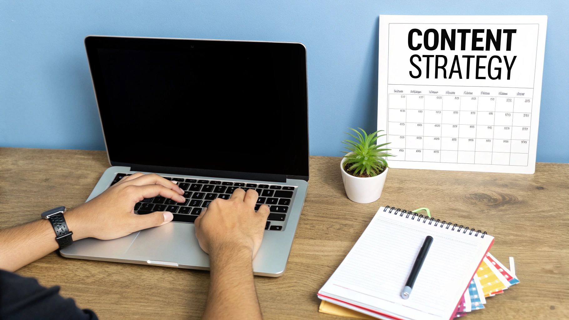 Person typing on a laptop next to a content strategy board and notebook on a wooden desk.