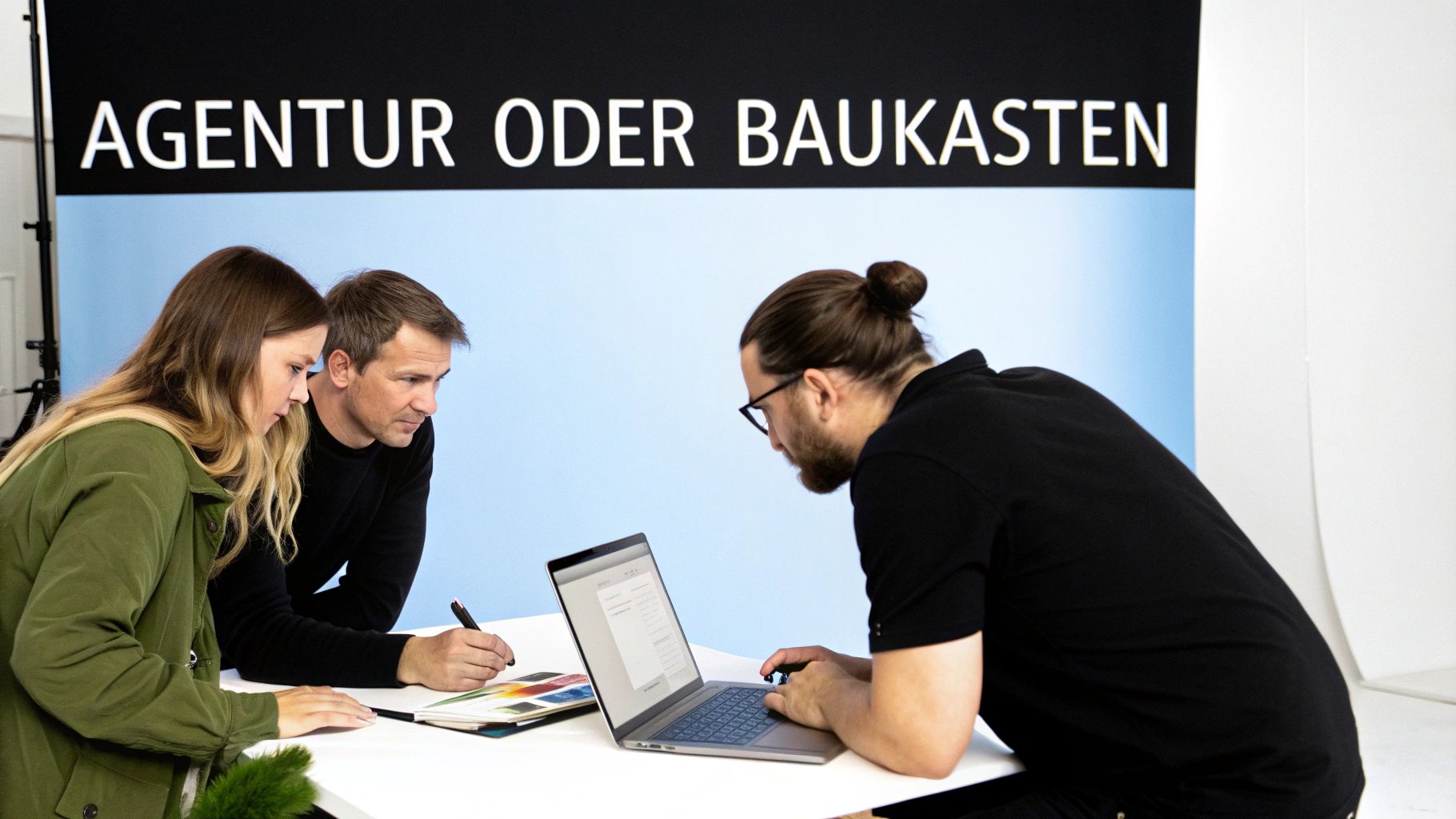 Drei Personen arbeiten an einem Tisch zusammen, besprechen Dokumente und nutzen einen Laptop. Im Hintergrund steht "AGENTUR ODER BAUKASTEN".