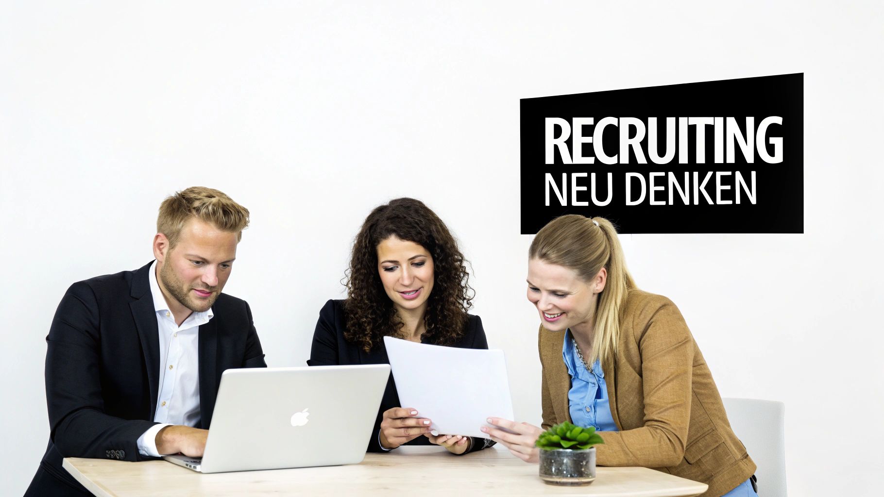 Drei Kollegen arbeiten gemeinsam an einem Tisch, betrachten Dokumente und einen Laptop. Im Hintergrund steht 'RECRUITING NEU DENKEN'.