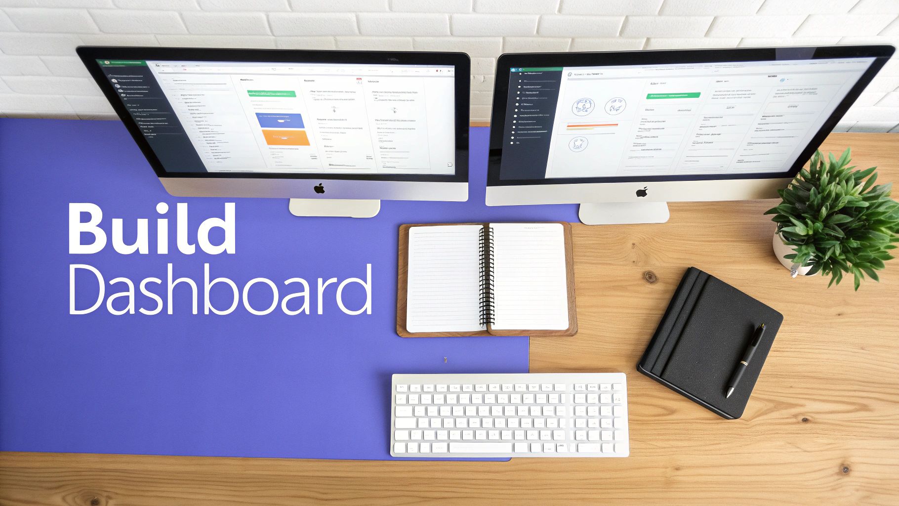 Modern desk setup with two computers displaying interactive dashboards, a keyboard, and notebooks on a blue mat.