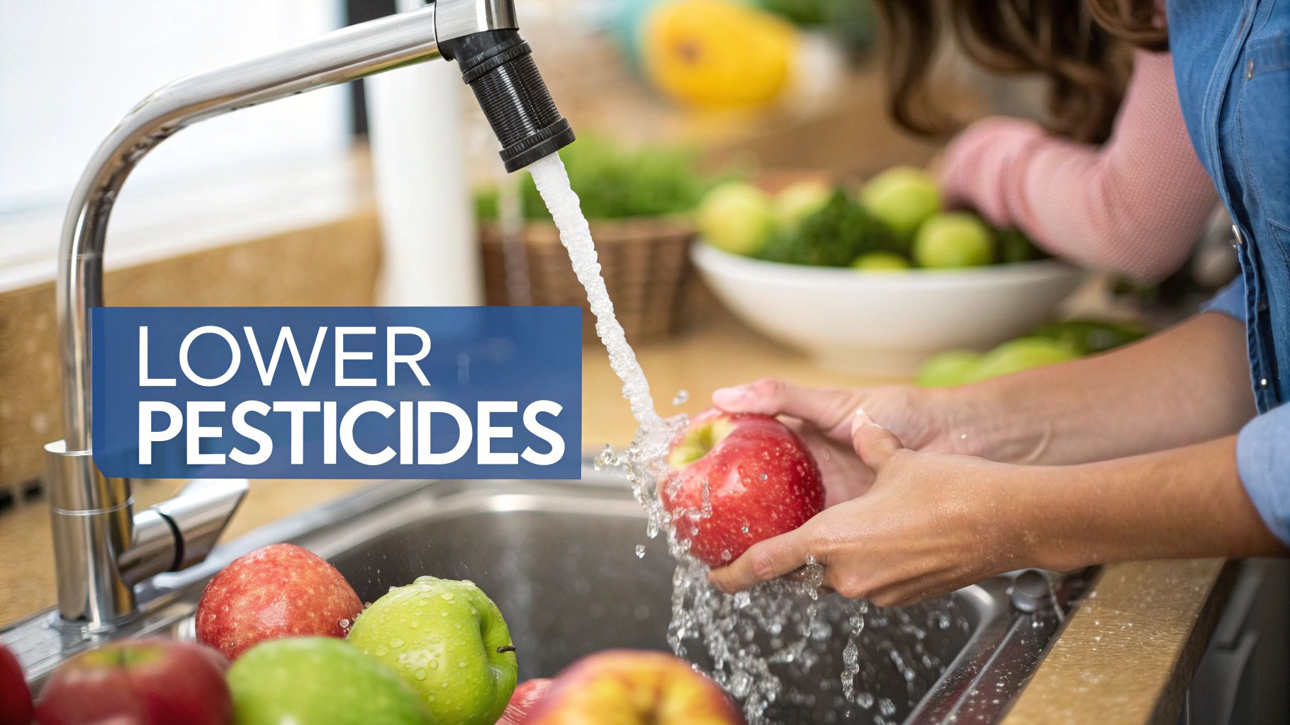 A person washes a red apple under running water in a kitchen sink, with 'LOWER PESTICIDES' text.