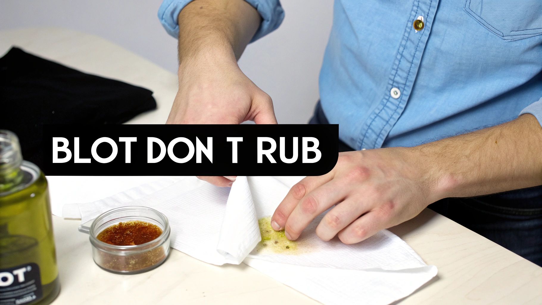 A person blots a green grease stain from white fabric using a paper towel, emphasizing blotting.
