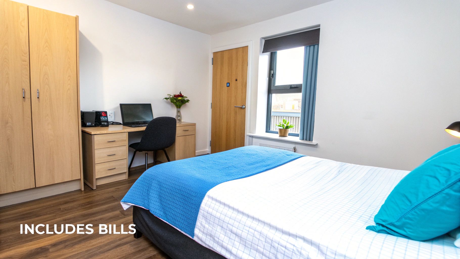 A brightly lit, tidy student bedroom featuring a bed, desk with laptop, chair, and wardrobe.