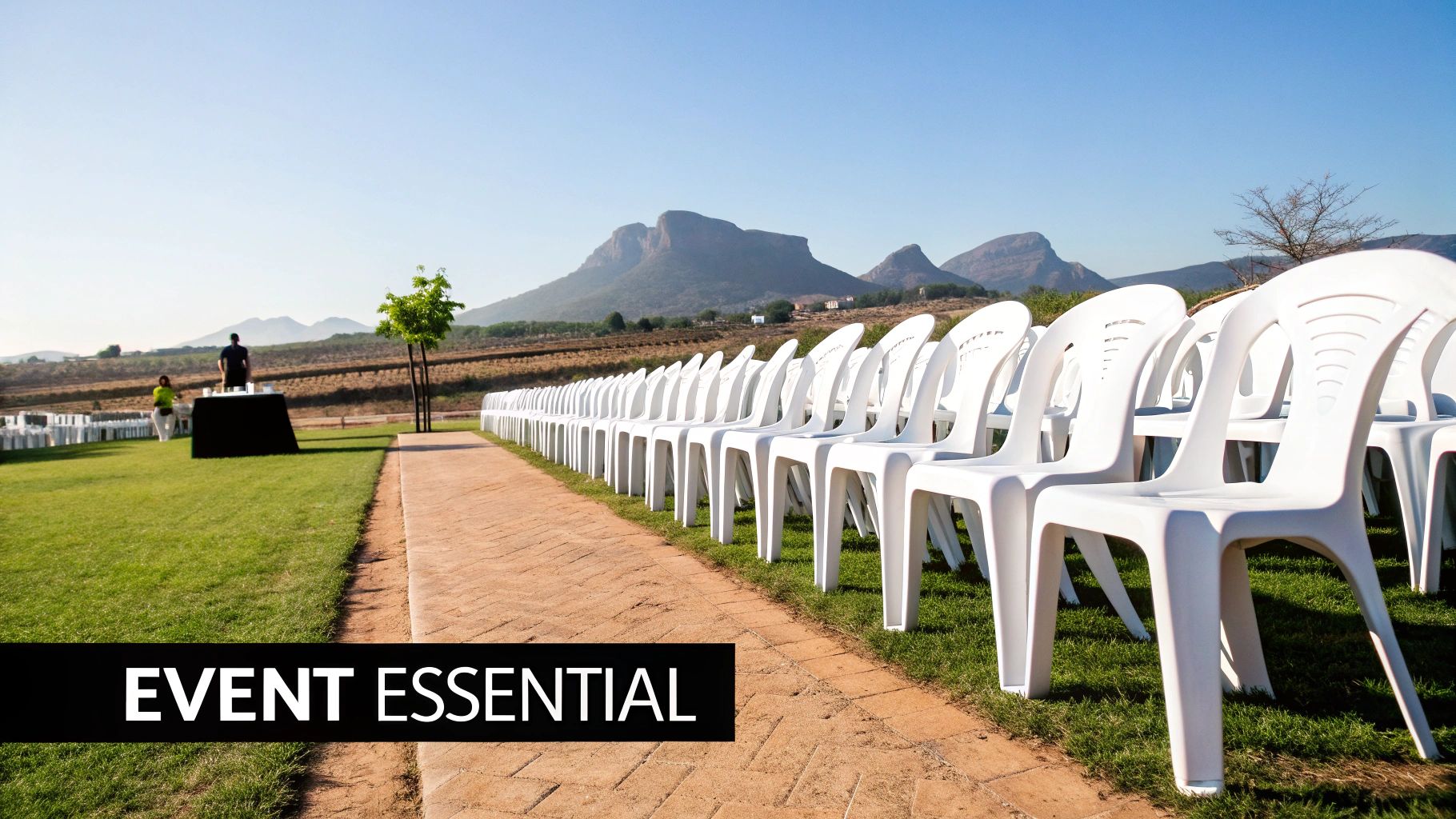 Rows of white plastic chairs arranged outdoors on grass for an event, with a mountain backdrop.