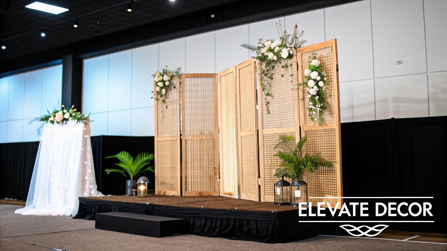 Elegant event stage decor featuring rattan screen dividers, white floral arrangements, and green plants.