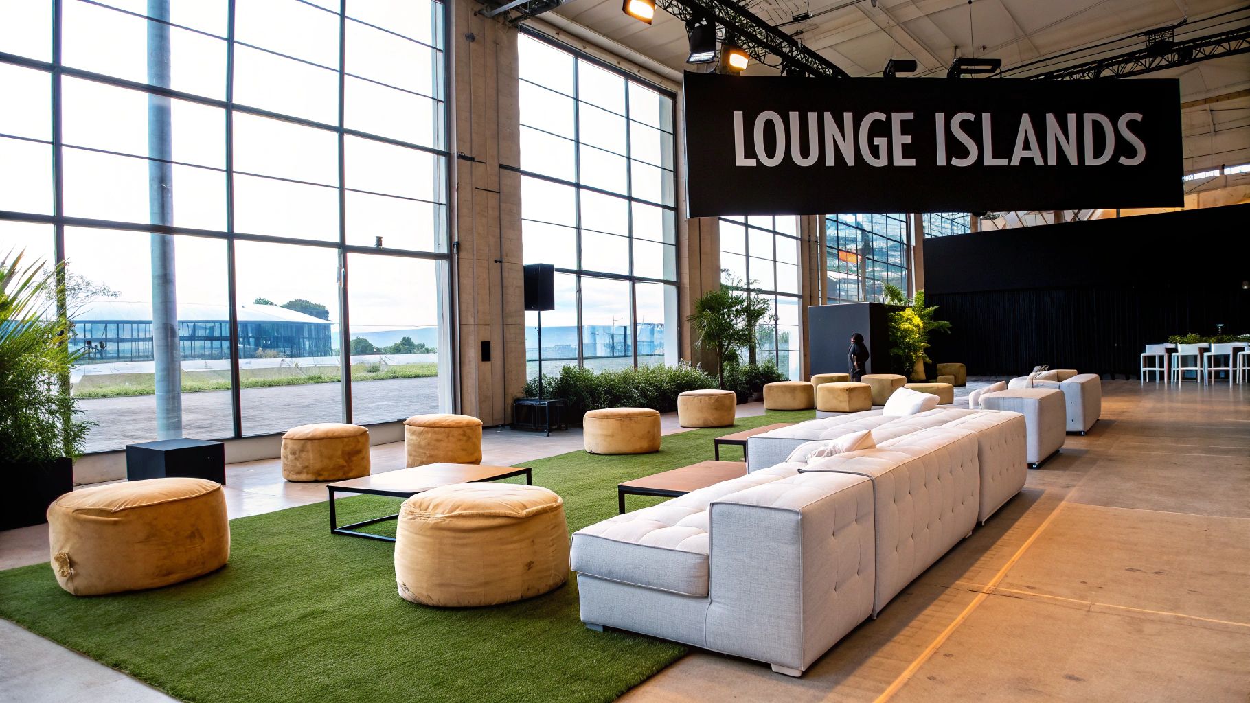 A modern lounge area with comfortable sofas, round yellow poufs, and large windows in an event space.