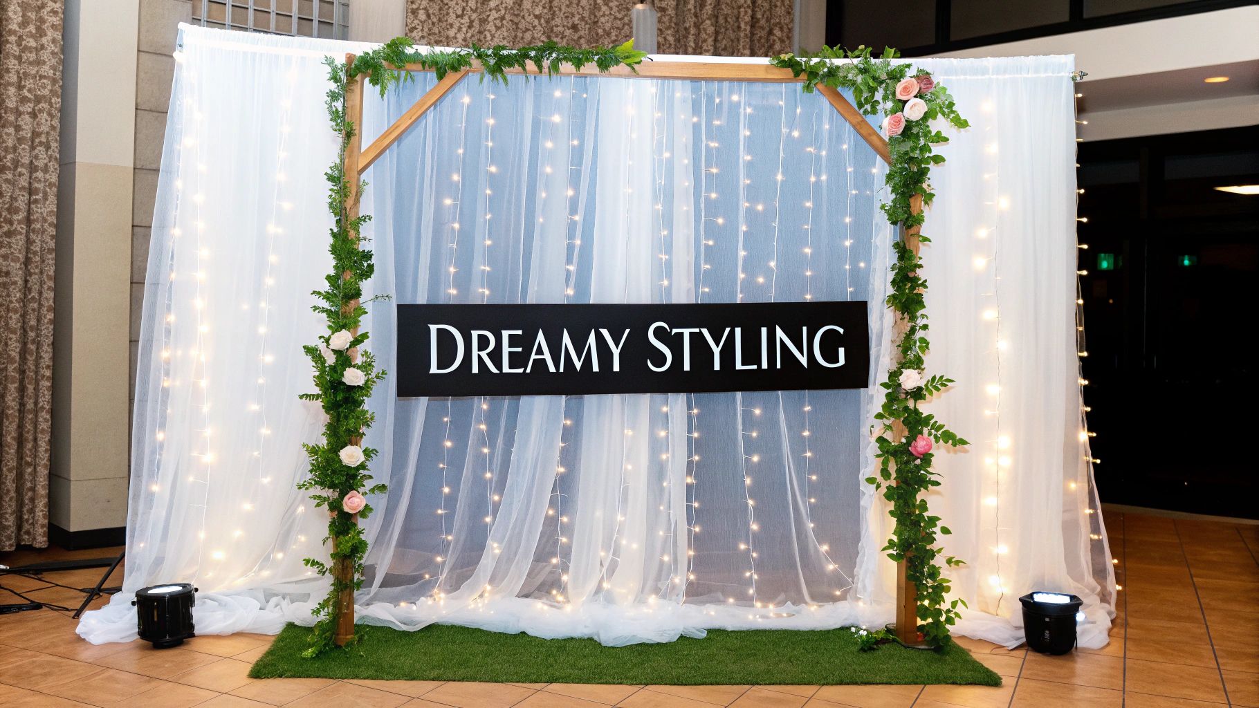 A dreamy photo backdrop with white sheer curtains, fairy lights, a floral wooden arch, and a 'DREAMY STYLING' sign.