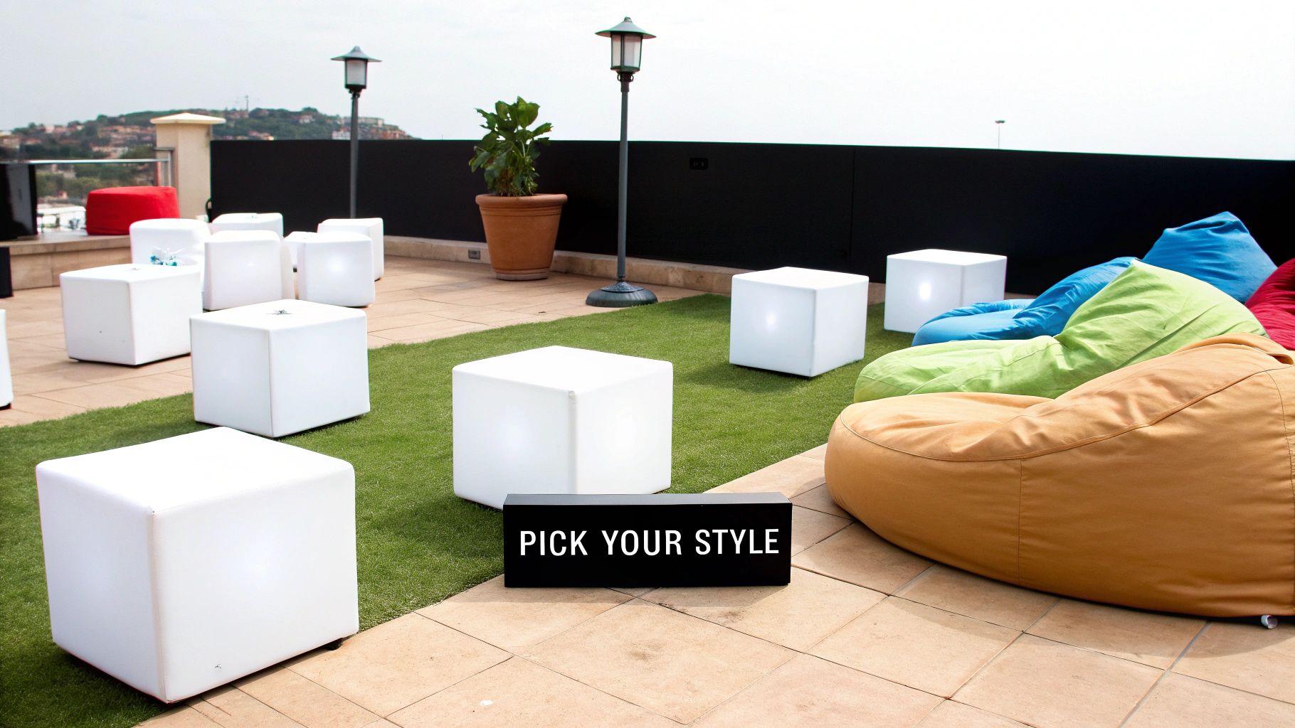 Outdoor rooftop lounge with glowing white cube furniture, colorful bean bags, and a 'Pick Your Style' sign.