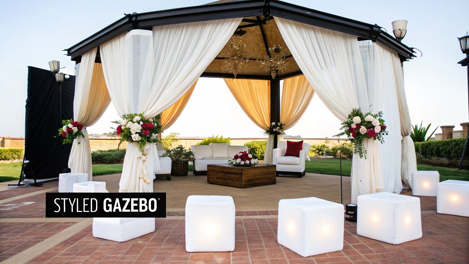 A beautifully styled outdoor gazebo with white drapes, floral decor, and elegant seating for an event.