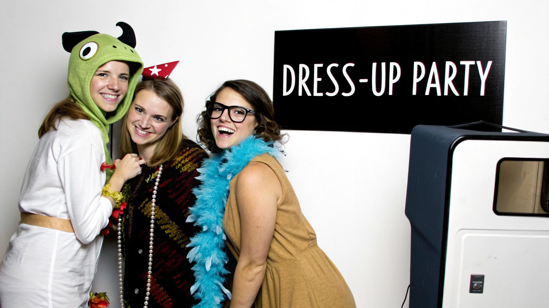 Three happy women in fun costumes at a dress-up party with a photo booth.
