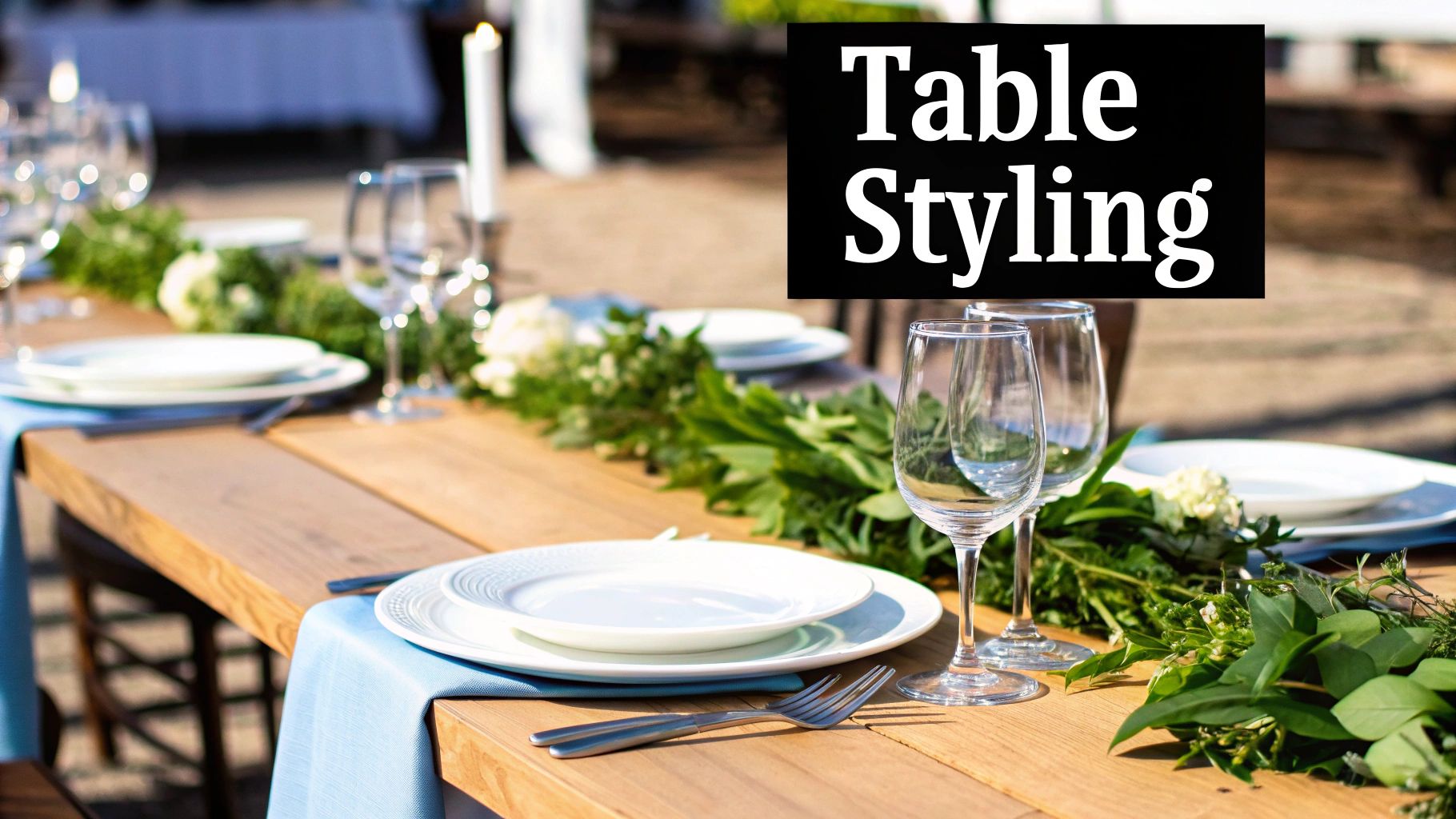 Elegant outdoor table styling with white plates, wine glasses, blue napkins and fresh greenery garland