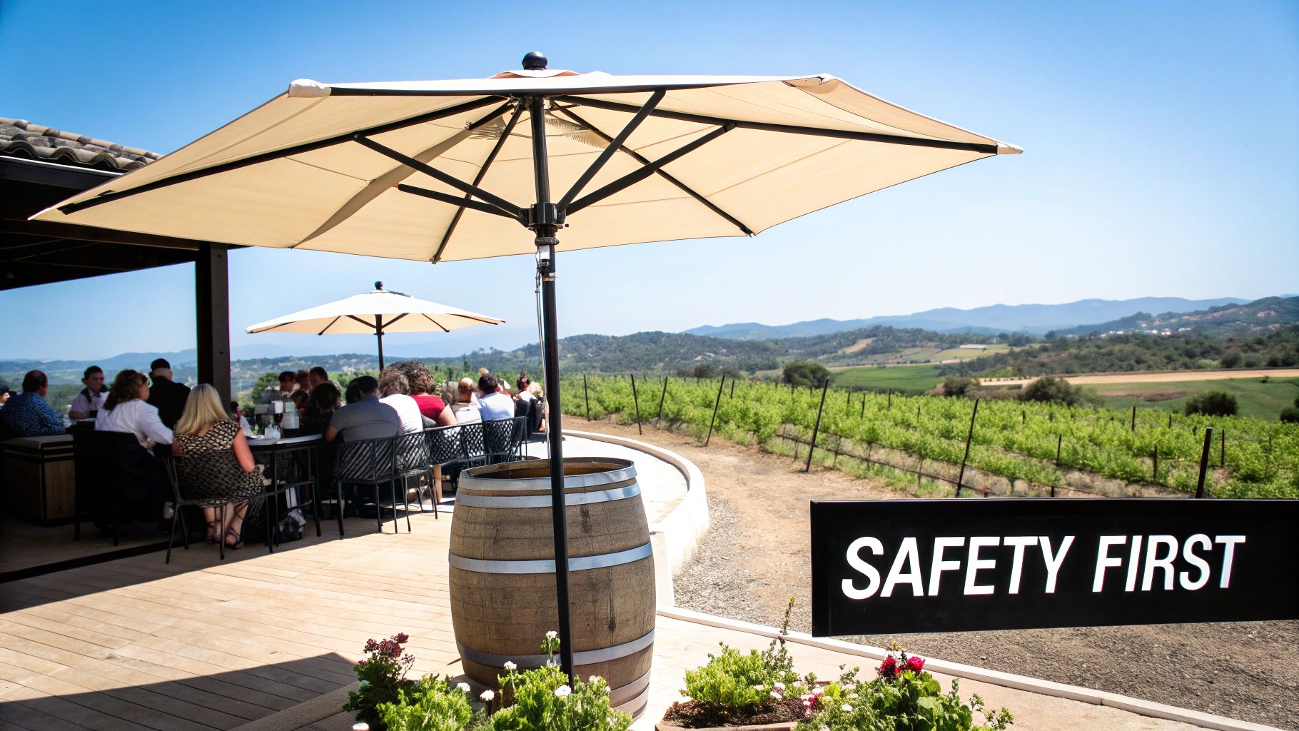 People dine on an outdoor patio under large umbrellas, overlooking a vineyard and mountains.