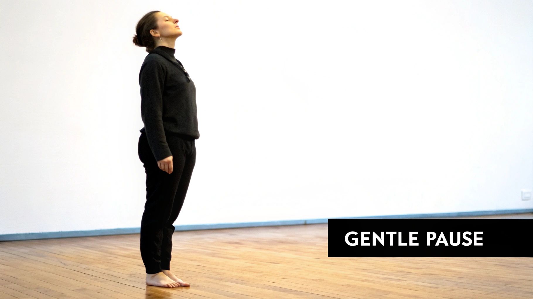 A woman sits peacefully in a calm, light-filled room, practicing gentle breathing.