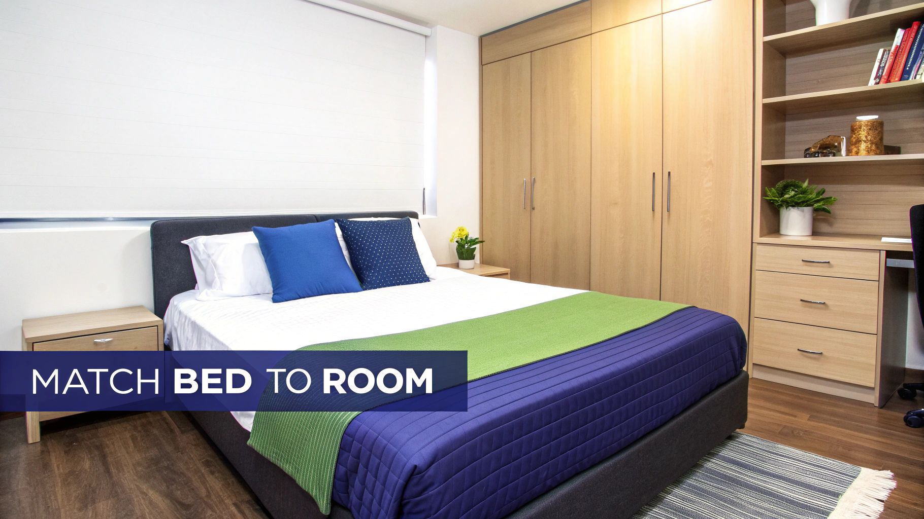 A modern bedroom features a bed with blue and green bedding, wooden furniture, and a rug.