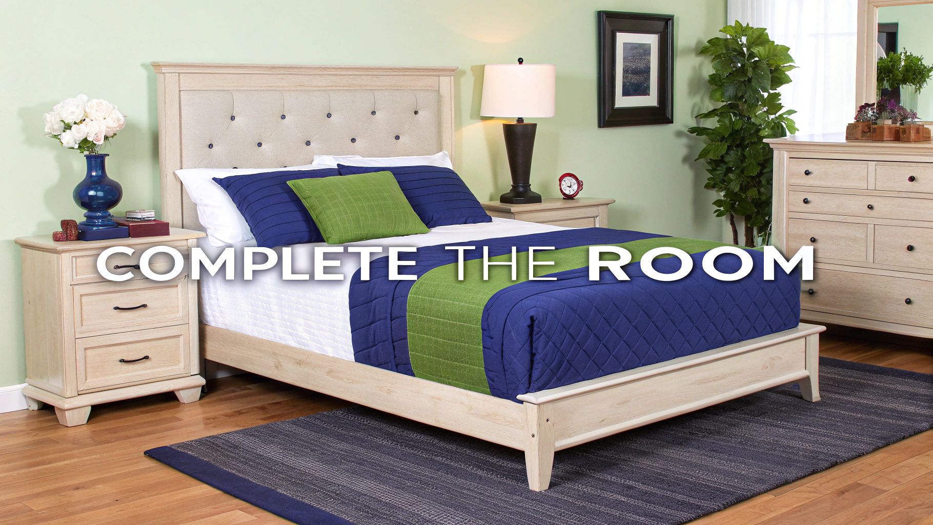 A light wood bed with an upholstered headboard, blue and green bedding, and complete bedroom furniture.