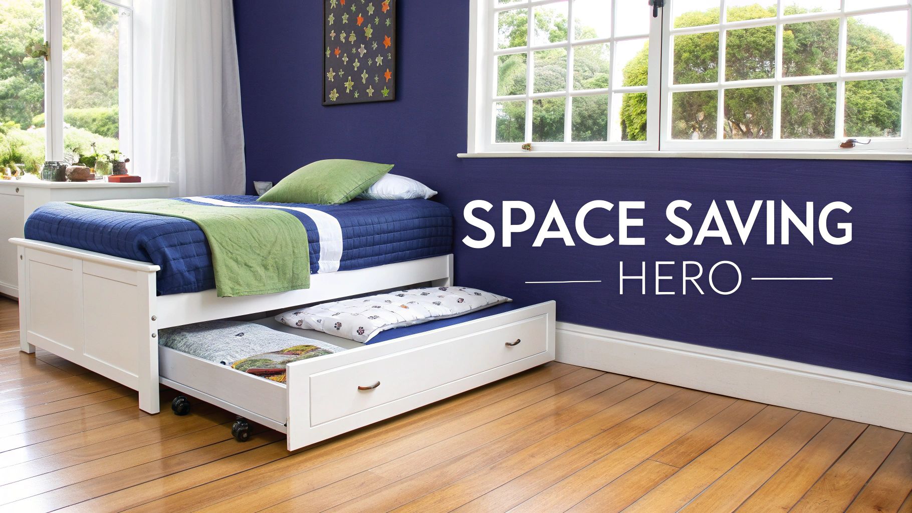 A white single bed with a trundle bed underneath, featuring blue and green bedding, in a room with blue walls and a wooden floor.
