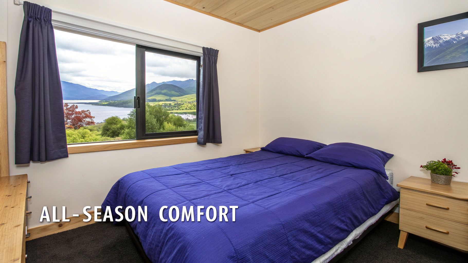 Bedroom with blue bedding overlooking scenic mountain lake view through large window in New Zealand