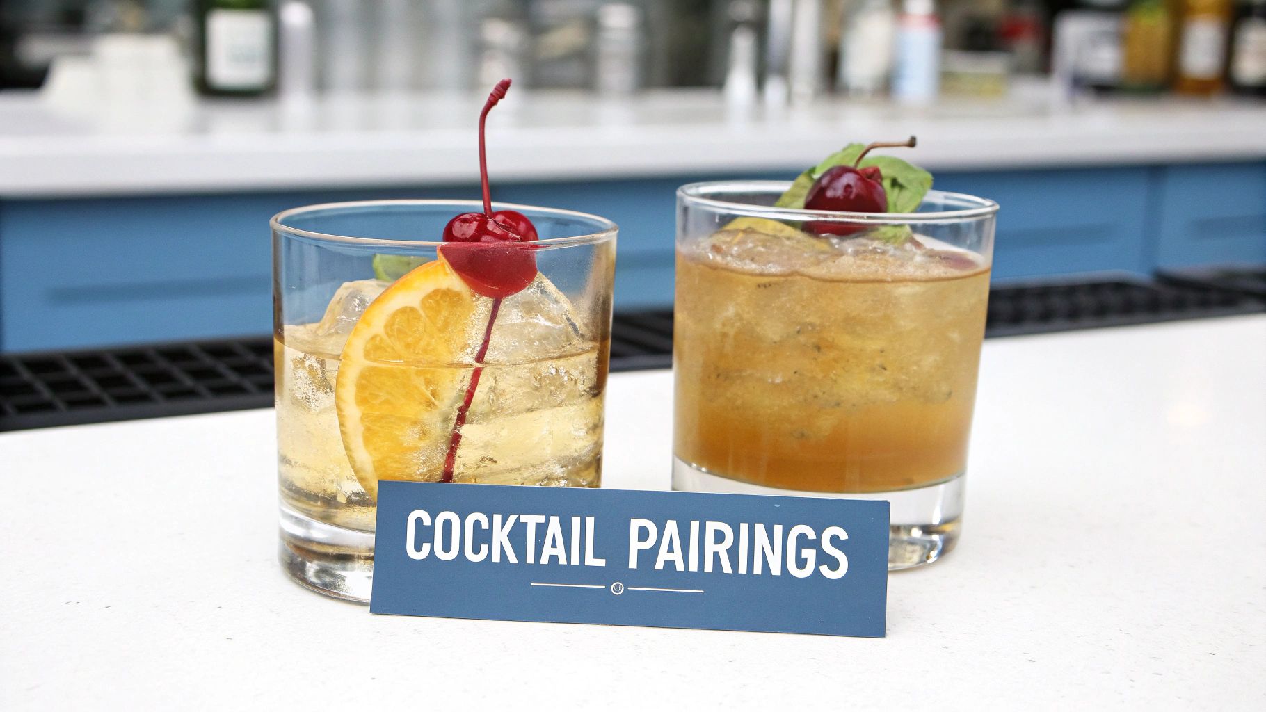 Two garnished cocktails, one with orange and cherry, the other with mint, on a bar counter with a 'Cocktail Pairings' sign.