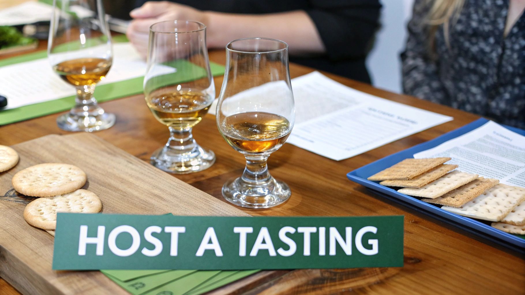 A close-up view of a whiskey tasting event setup with glasses, crackers, and a 'Host a Tasting' sign.