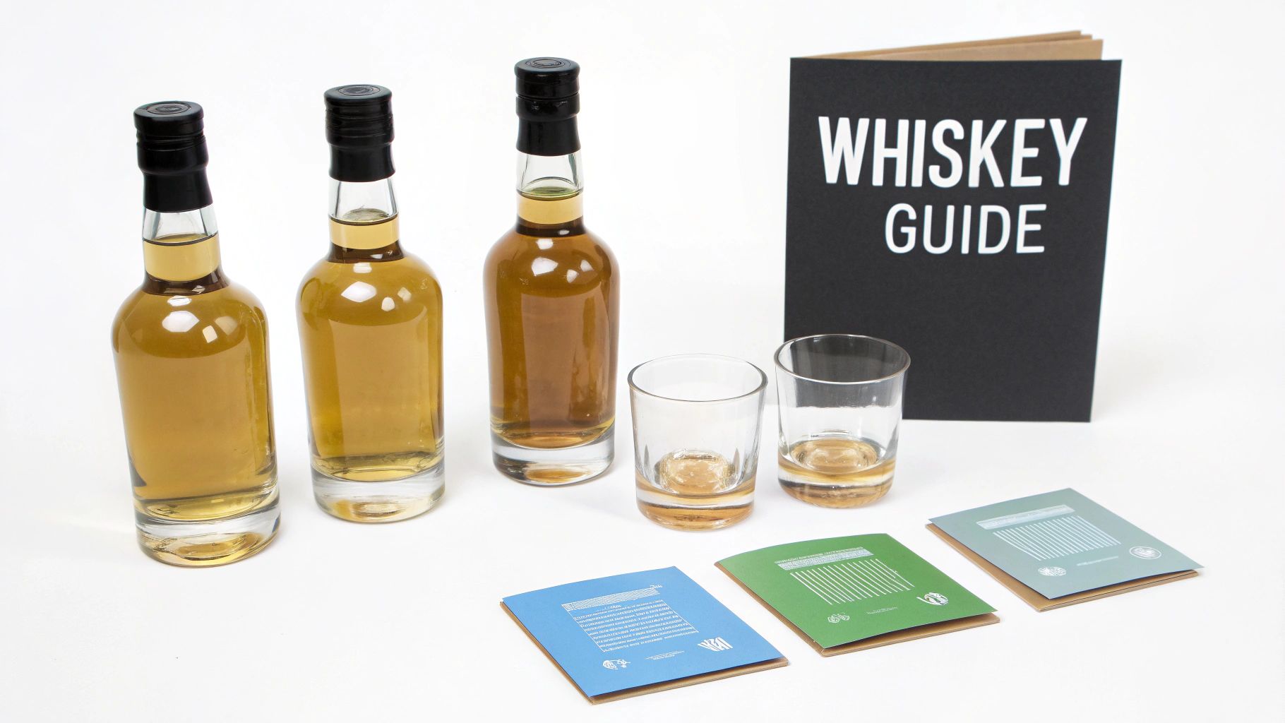 A collection of bourbon, rye, and scotch whiskey bottles and glasses arranged on a wooden surface.