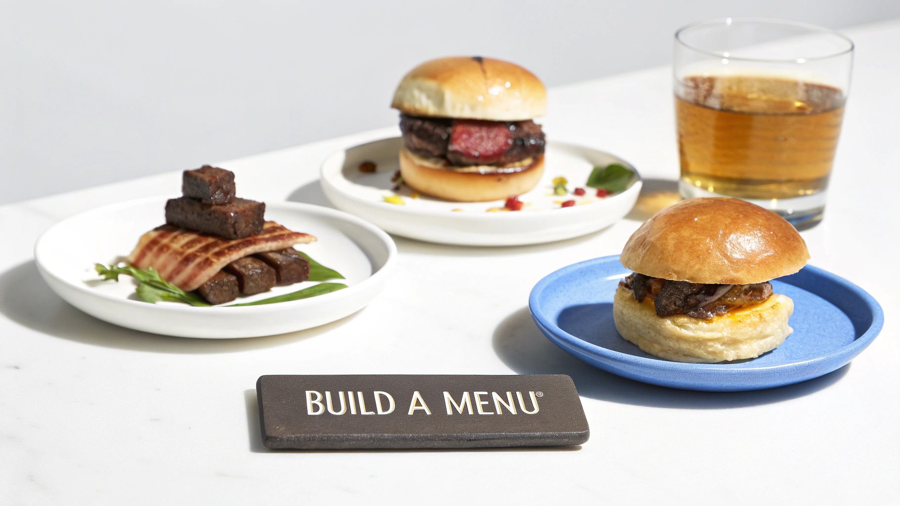 Three gourmet meat dishes, including sliders and stacked pork, served with whiskey and a 'Build A Menu' sign.