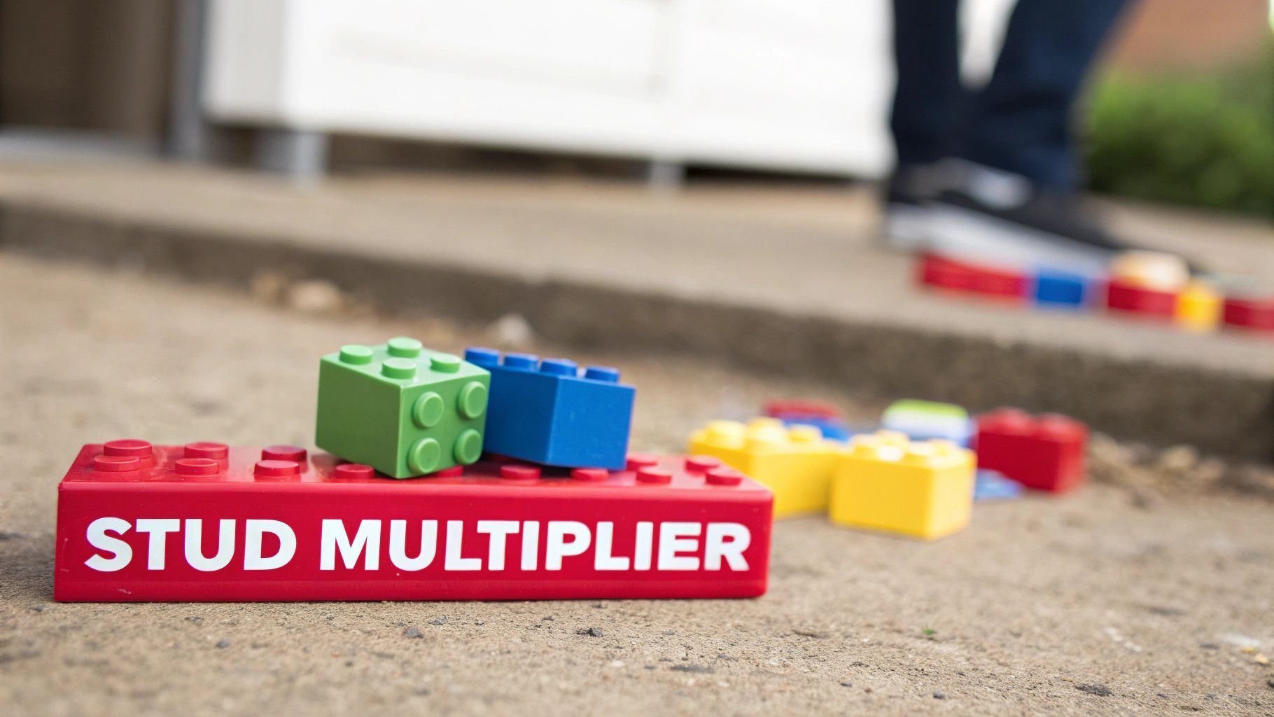 A red LEGO brick labeled 'STUD MULTIPLIER' with green and blue bricks on top, lying on concrete.