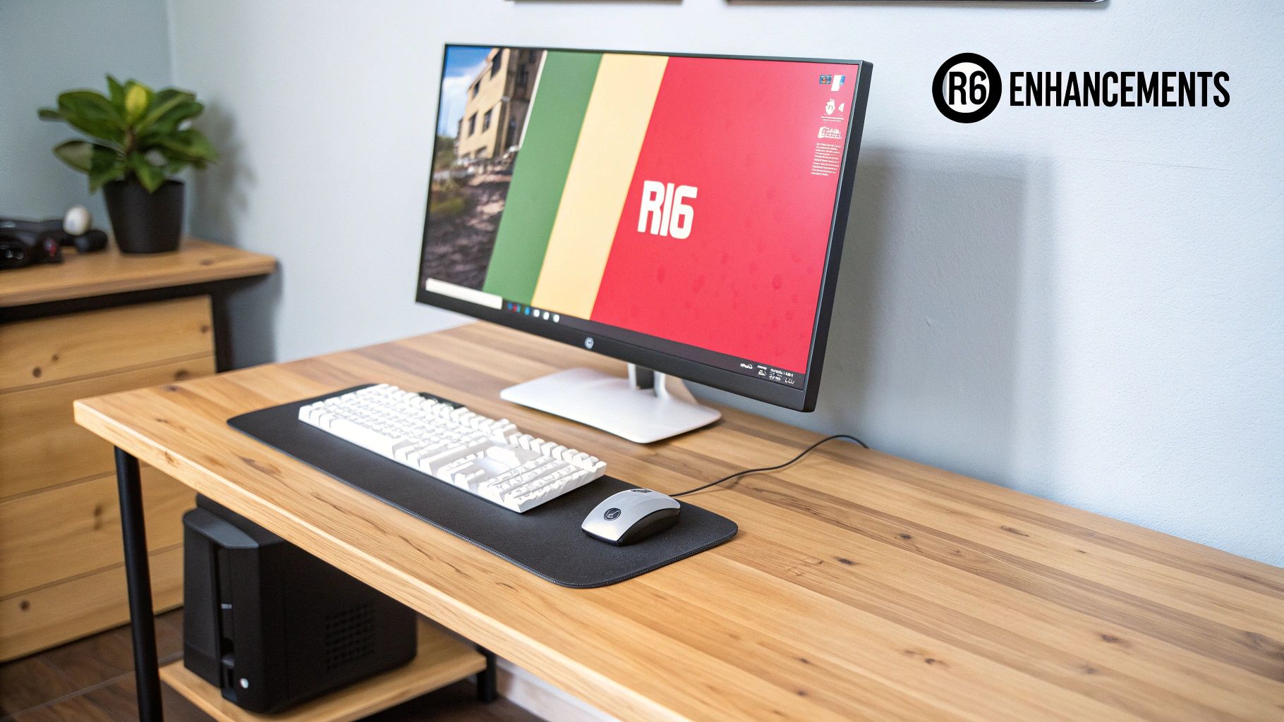 A modern gaming desk setup featuring a monitor showing R16, white keyboard, mouse, and a compact PC.