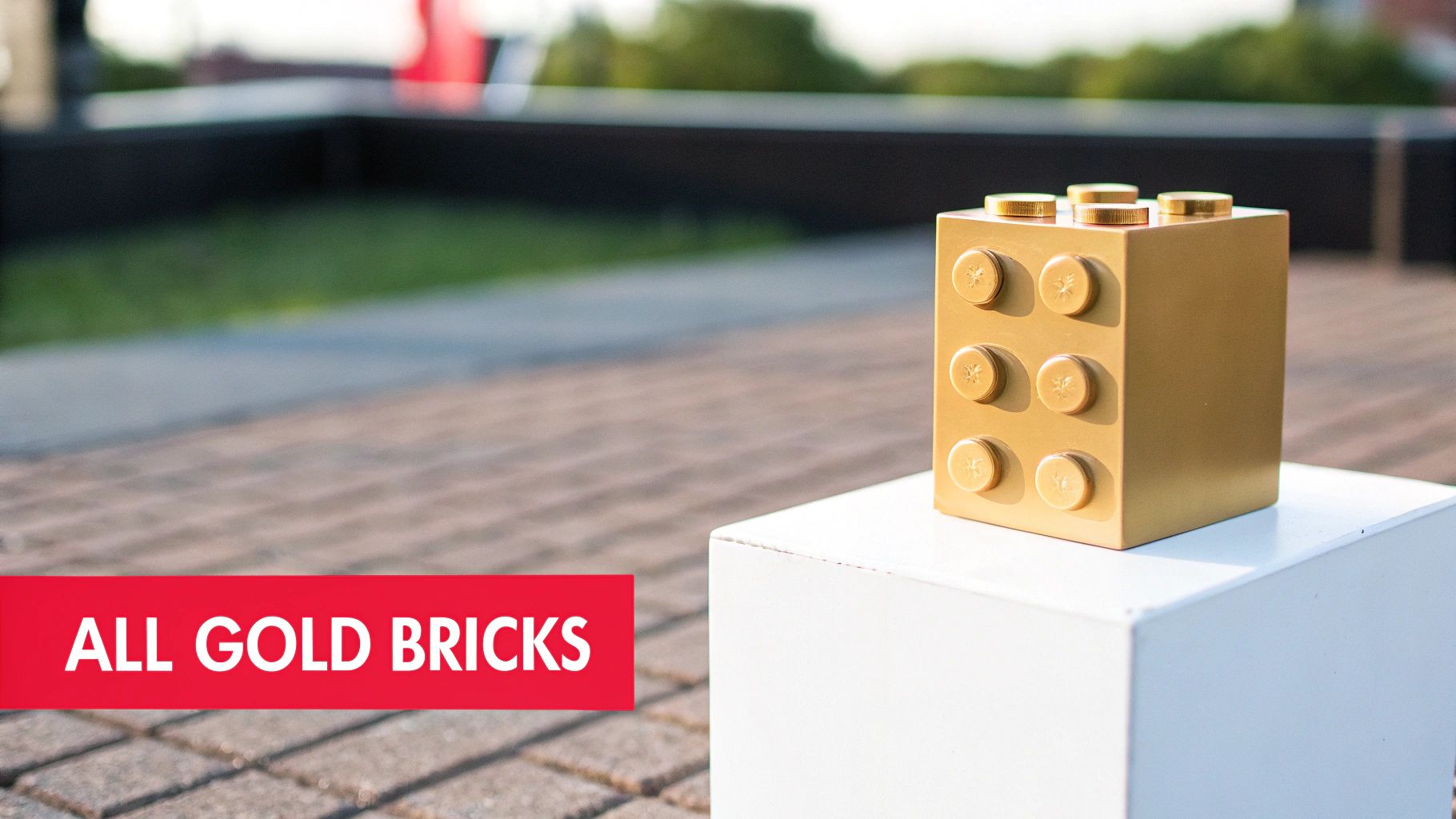 A large golden Lego brick with starburst studs sits on a white pedestal outdoors.