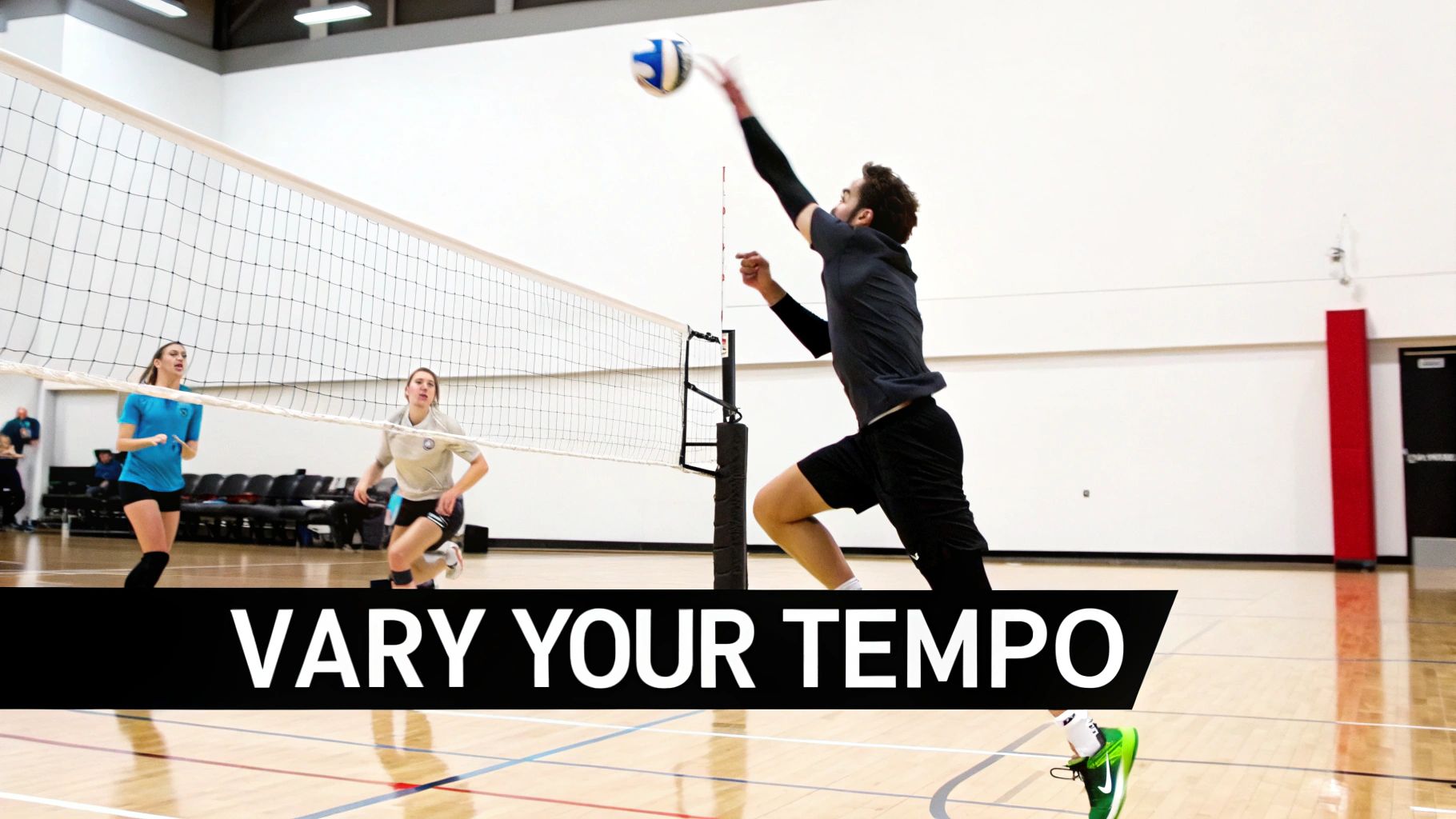 A male volleyball player spikes the ball over the net during an indoor game, with female players on defense.