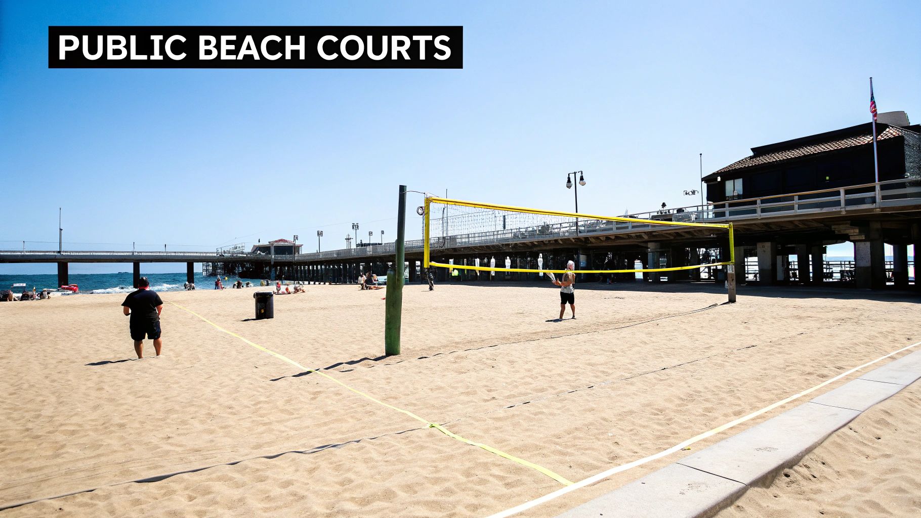 A bright sunny day on a sandy public beach with a yellow volleyball net set up.