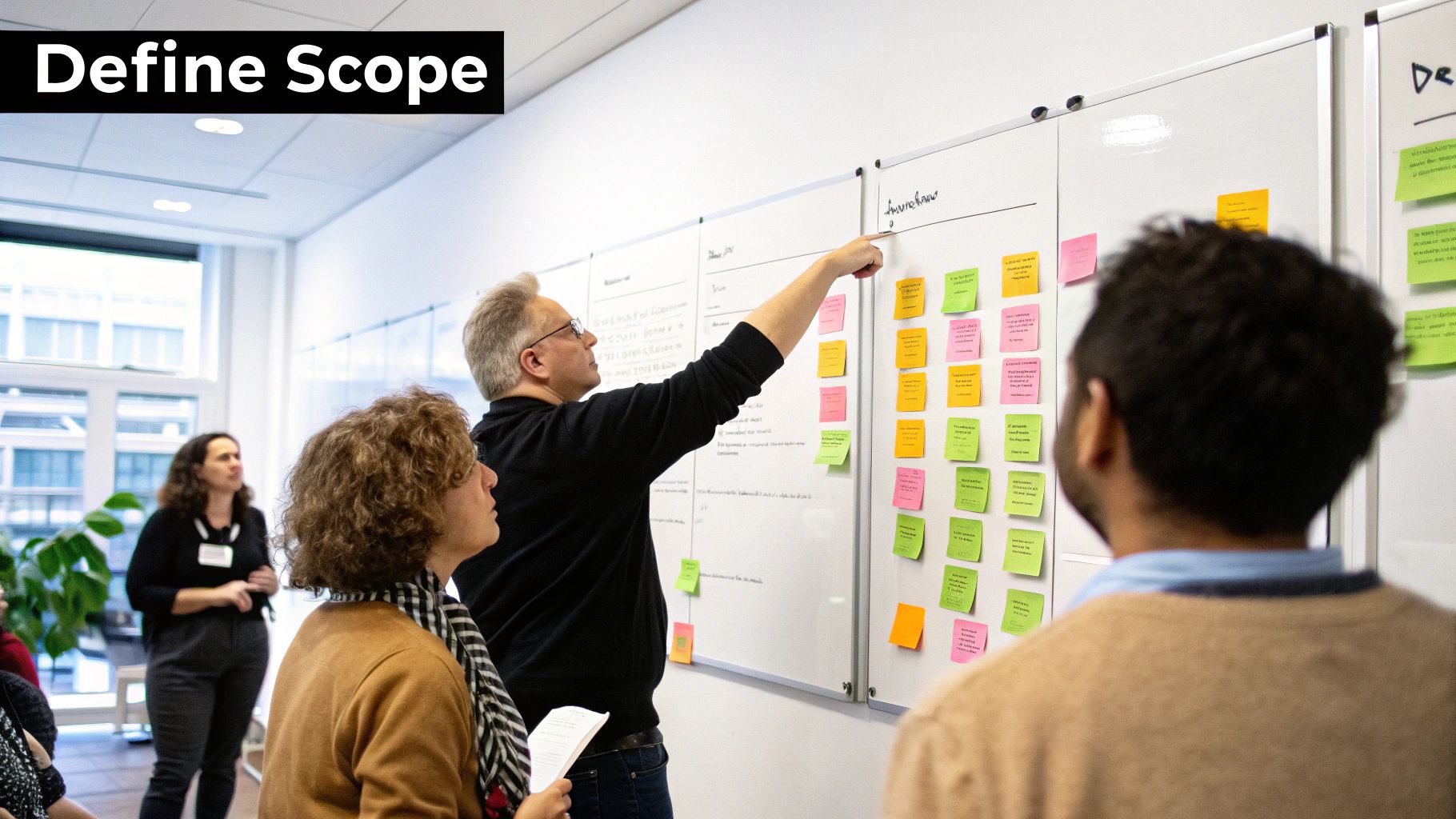 A man points to a whiteboard covered with sticky notes during a project scope definition meeting.