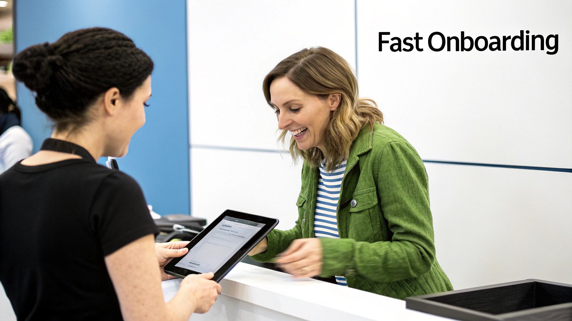 A smiling woman completes a fast digital onboarding process with assistance from another person holding a tablet.