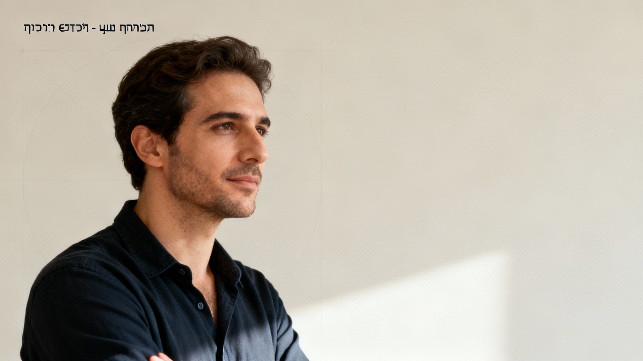 גבר צעיר עם חולצה כהה מביט הצידה בהבעת מחשבה, על רקע בהיר ומודרני.