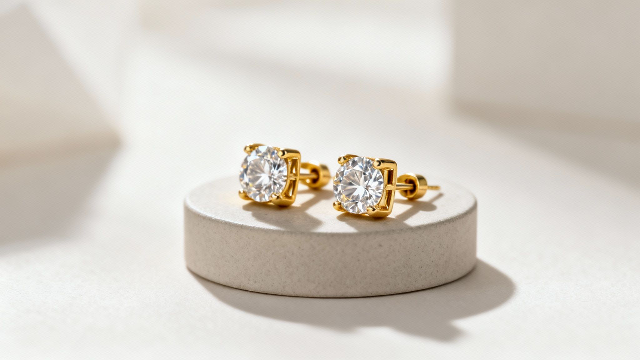 זוג עגילי זהב צמודים עם אבנים מבריקות על מעמד עגול בהיר, בתאורה רכה ואלגנטית.