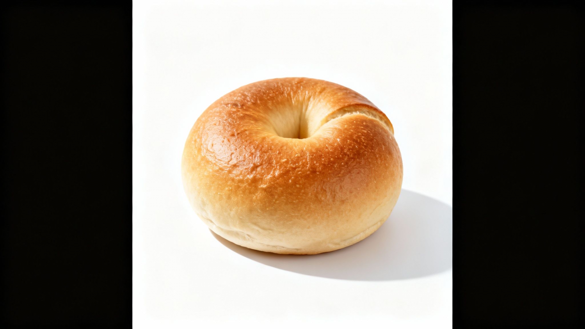 בייגל חלק ושחום-זהוב מונח על משטח לבן, מטיל צל עדין.