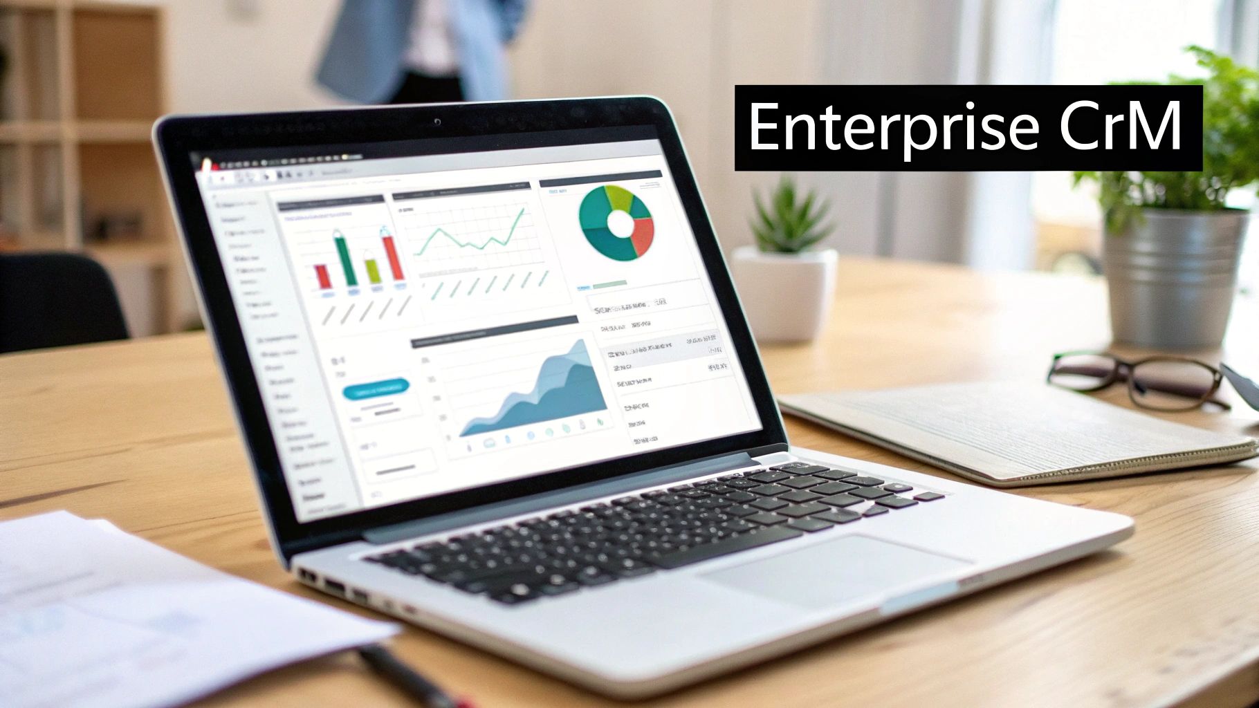 A laptop on a wooden desk displaying an Enterprise CrM dashboard with charts and graphs.