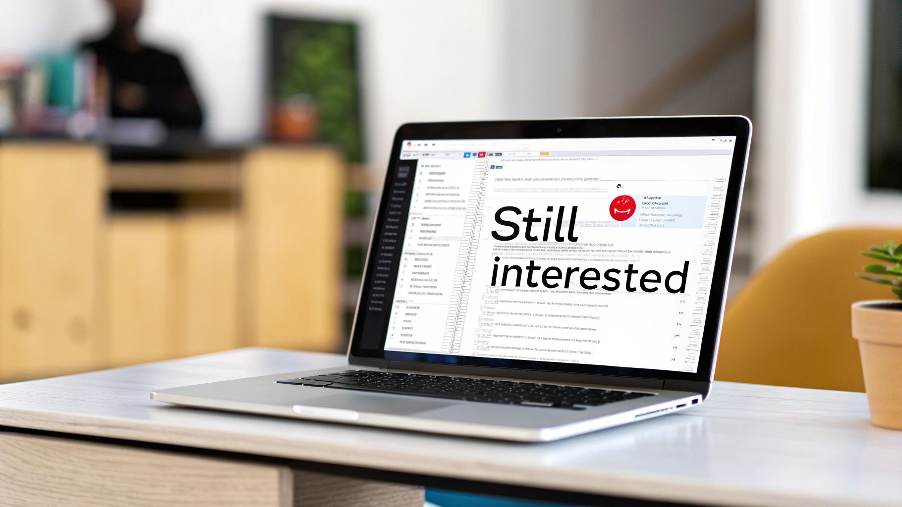 A laptop on a white desk displaying a 'Still interested' follow-up email, with a blurred office background.
