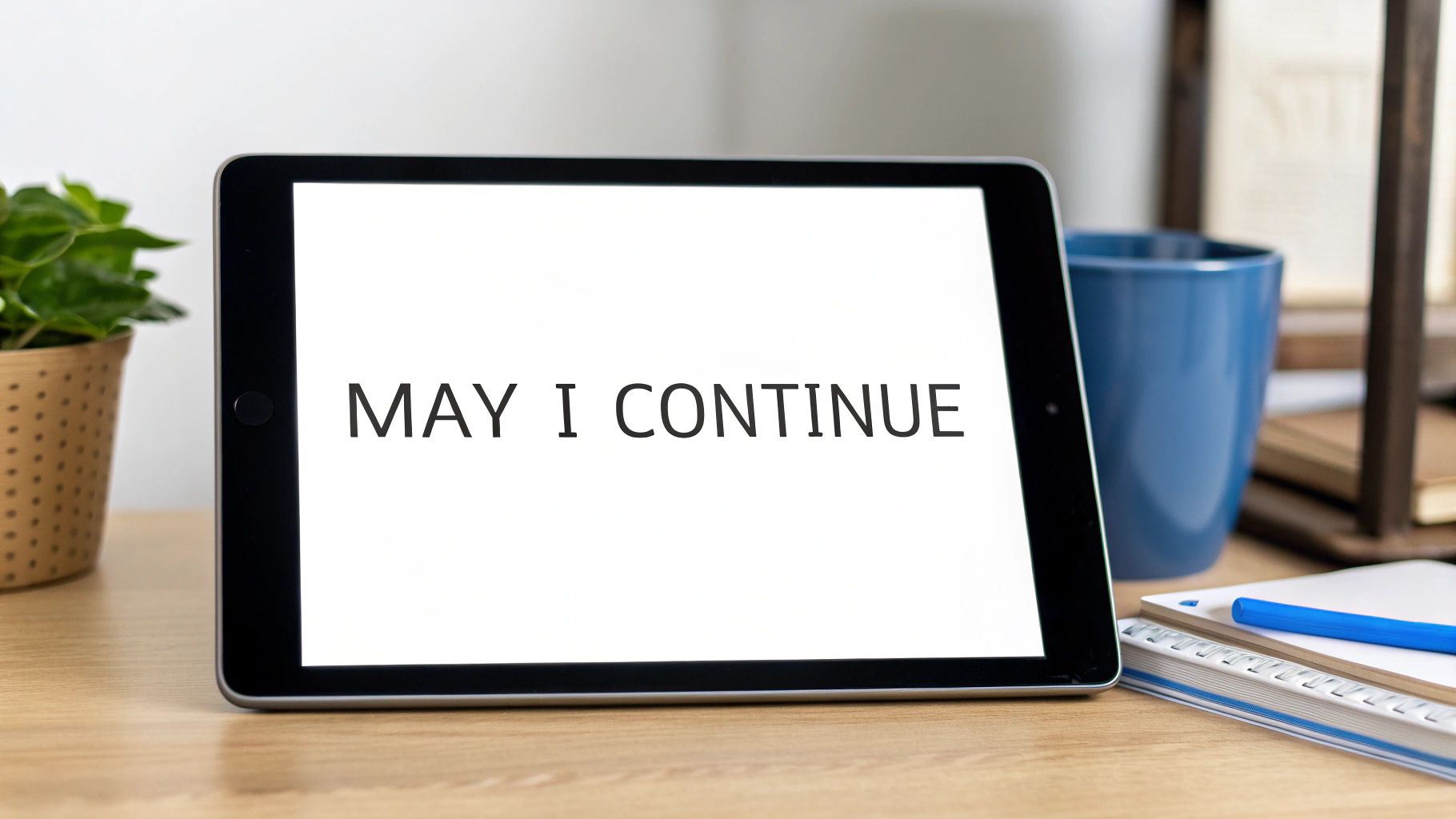 A tablet on a wooden desk displays the text 'MAY I CONTINUE', with a plant and mug.